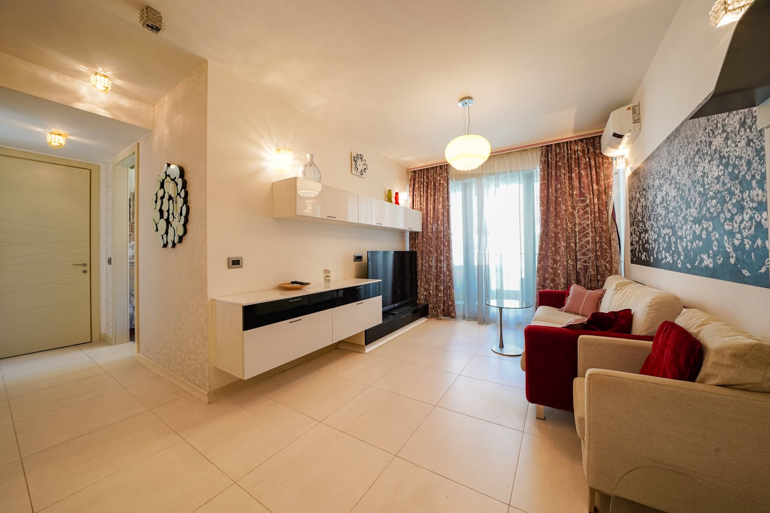 Modern living room with white furniture and a red sofa in an apartment, Budva, Montenegro. Bright interior with a panoramic window.
