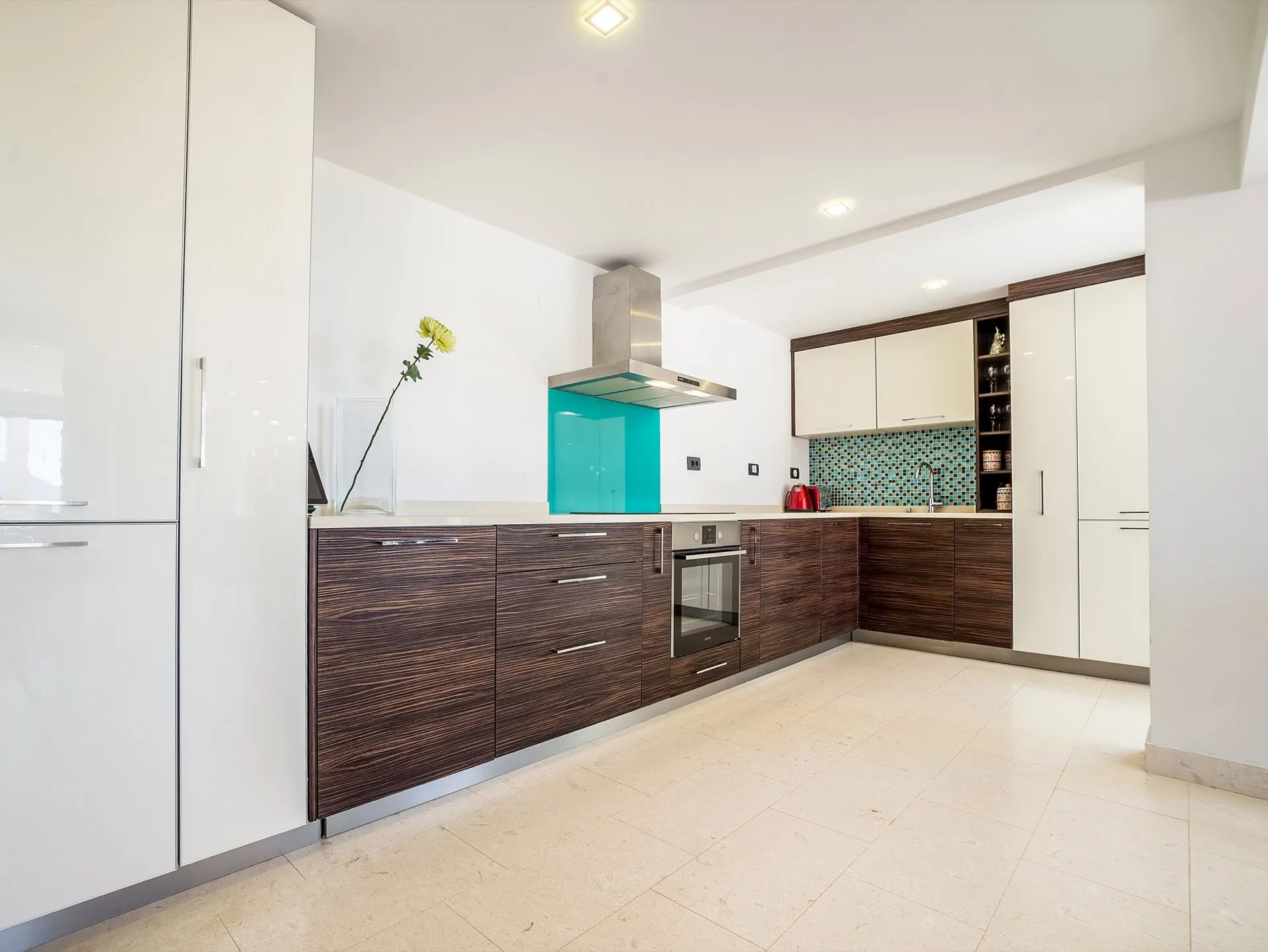 Modern kitchen featuring dark wood cabinetry, glossy white units, a turquoise mosaic backsplash, and stainless steel appliances.
