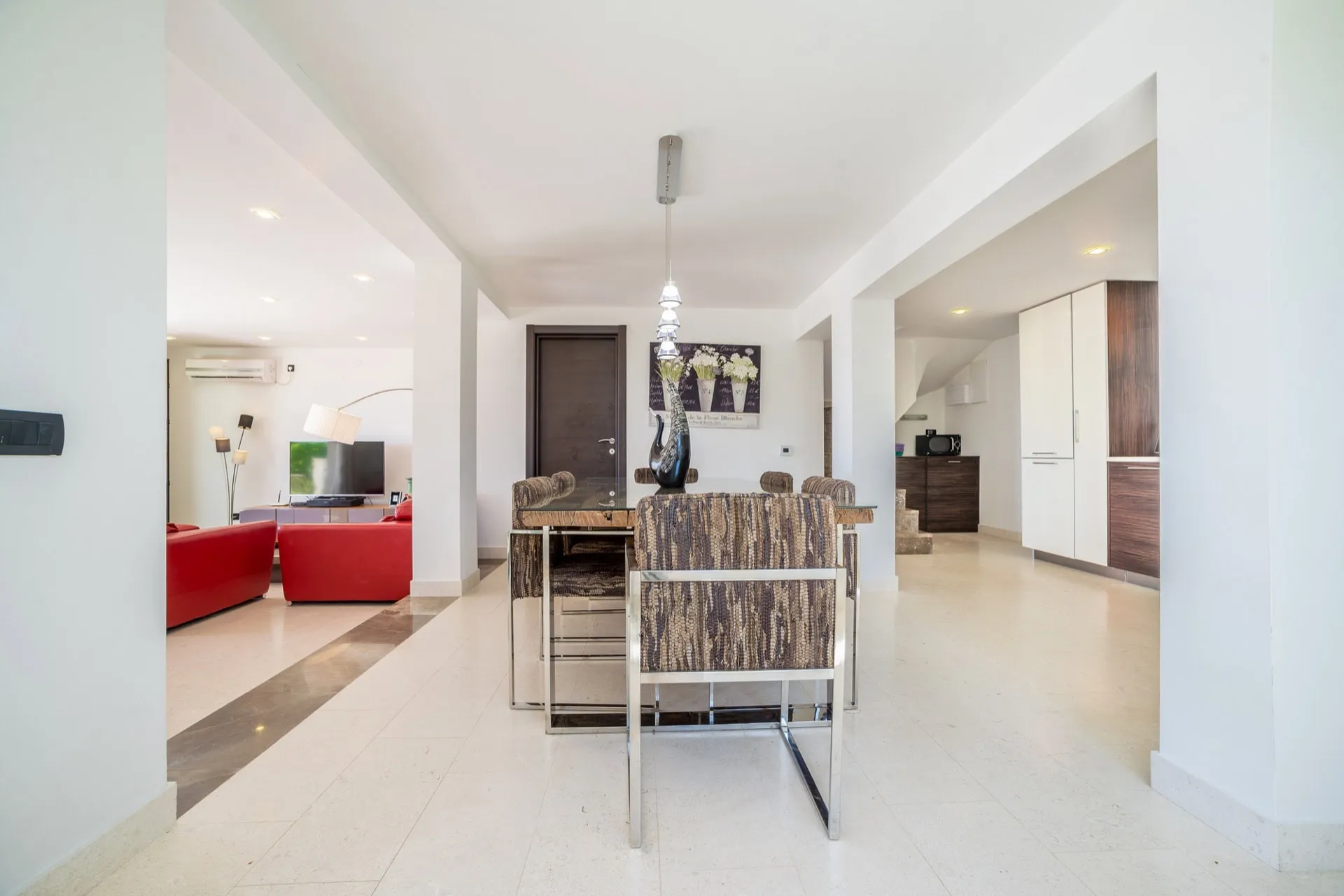 Open plan space featuring a dining table with patterned chairs, red sofa in the living area, and kitchen visible to the right.
