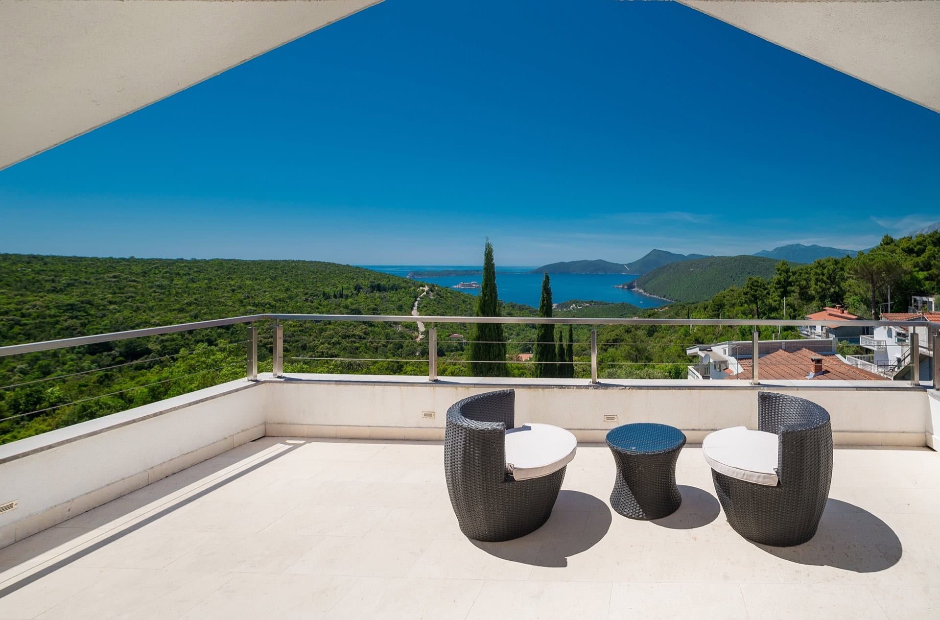 Villa terrace in Zanjice, Montenegro: rattan furniture, panoramic views of the sea, mountains, and pine forest.