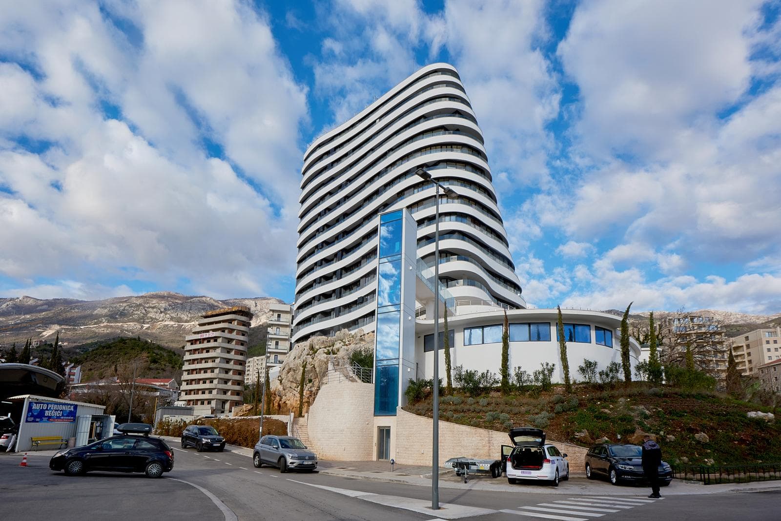 Modern multi-story residential complex with panoramic balconies in Bečići, Montenegro, against a mountain backdrop.