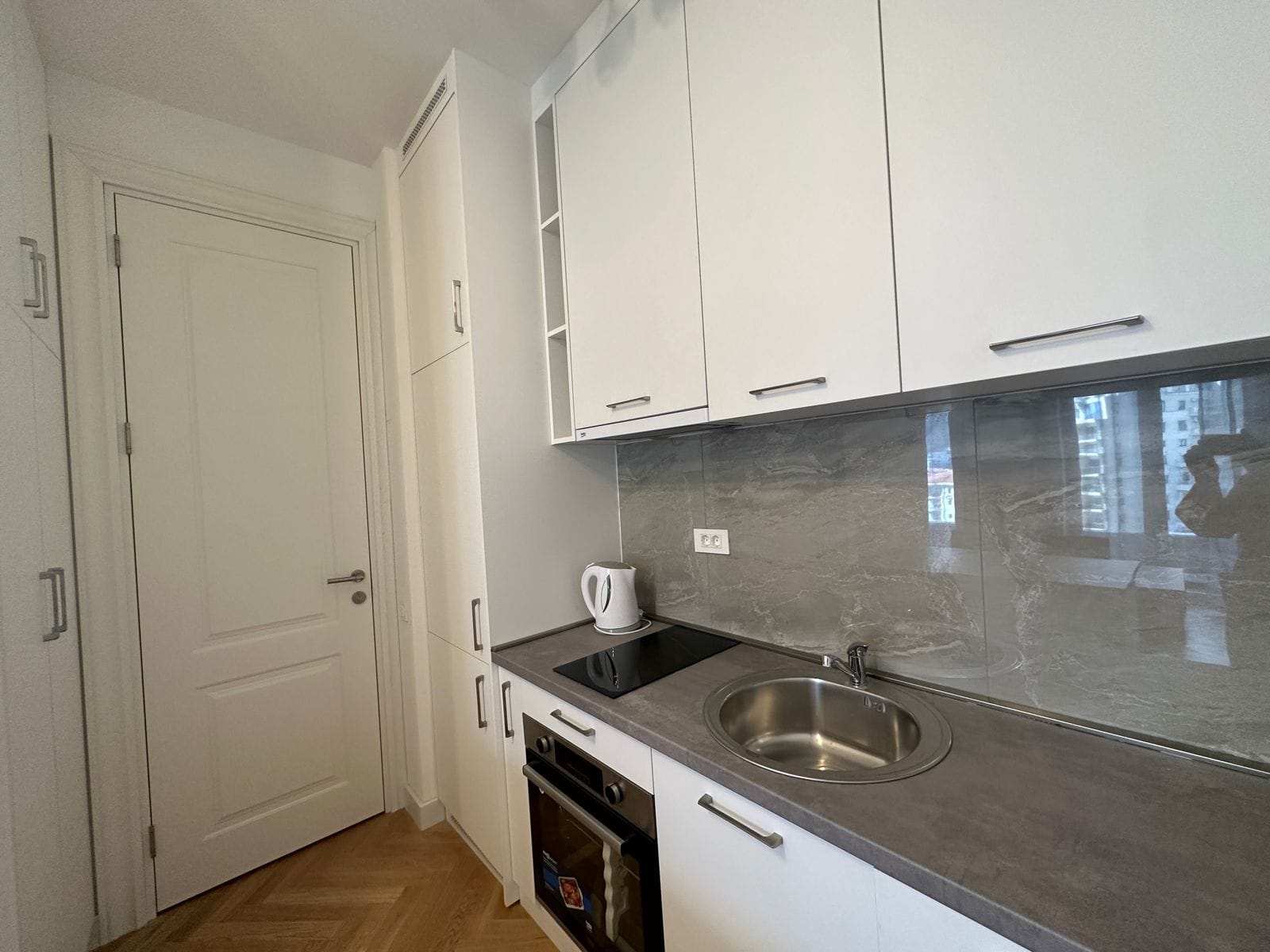 Modern white kitchen with a gray backsplash in an apartment in Bečići, Montenegro: built-in appliances and a bright interior.
