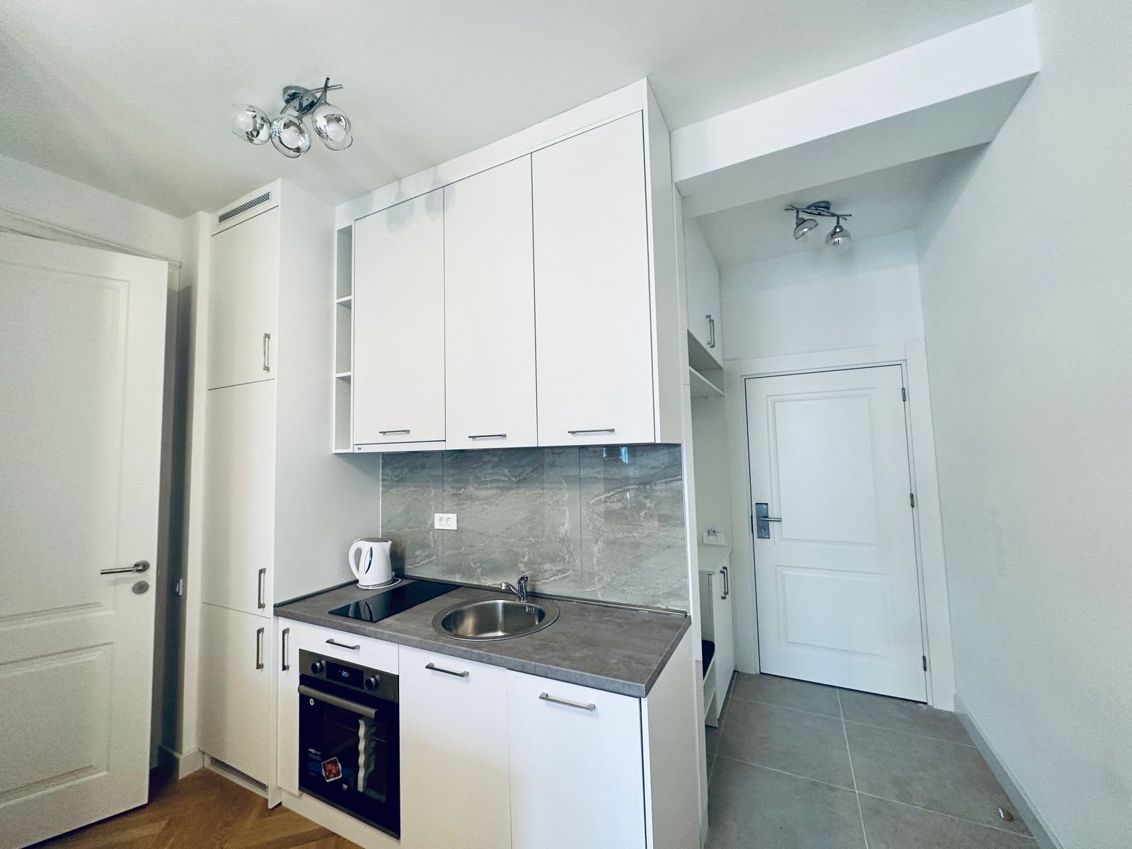 Modern white kitchen in an apartment in Bečići, Montenegro: built-in appliances, stone countertop, and marble-look backsplash.