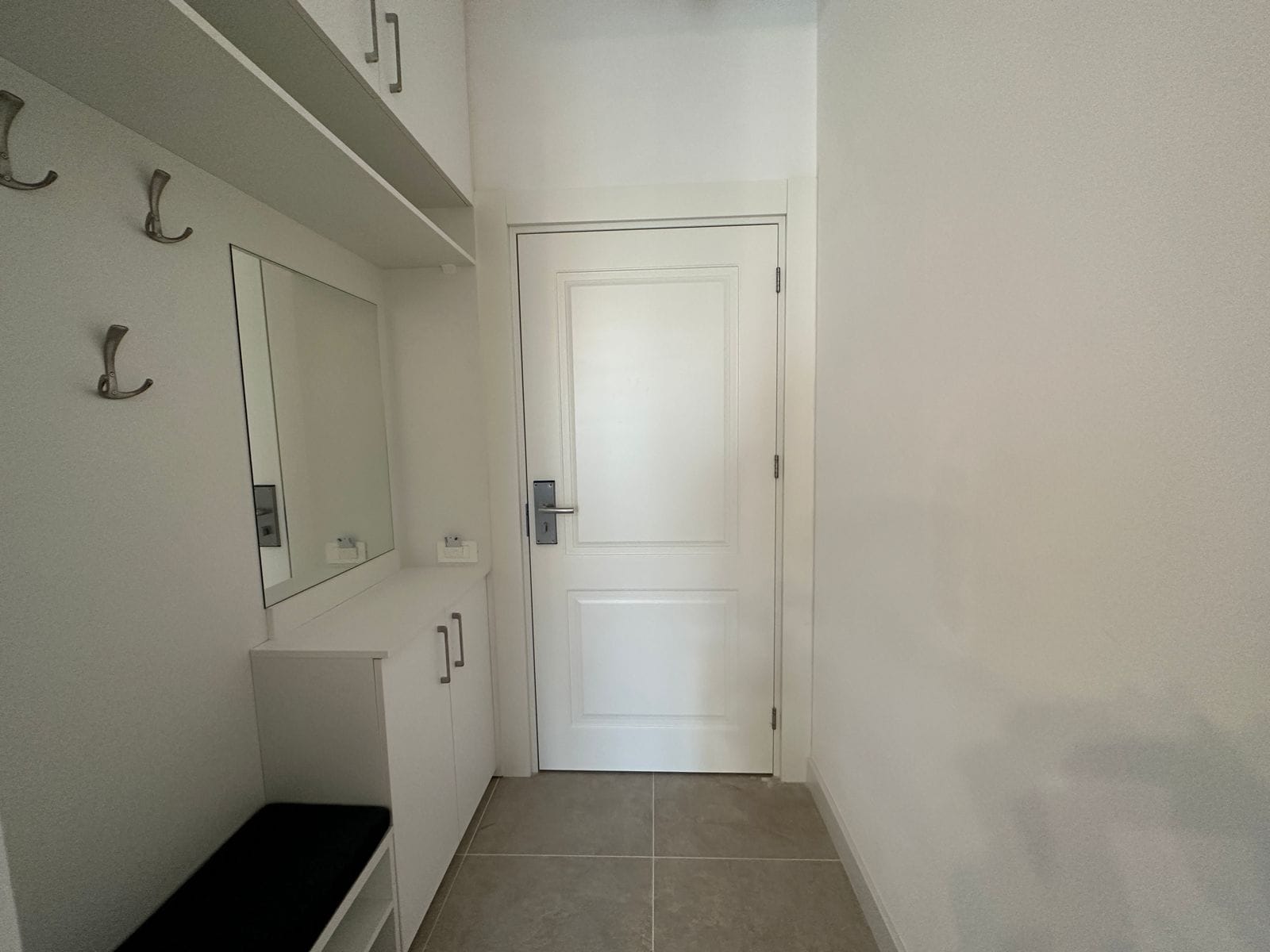 Bright hallway with white furniture, a mirror, and an entrance door in an apartment, Becici, Montenegro.