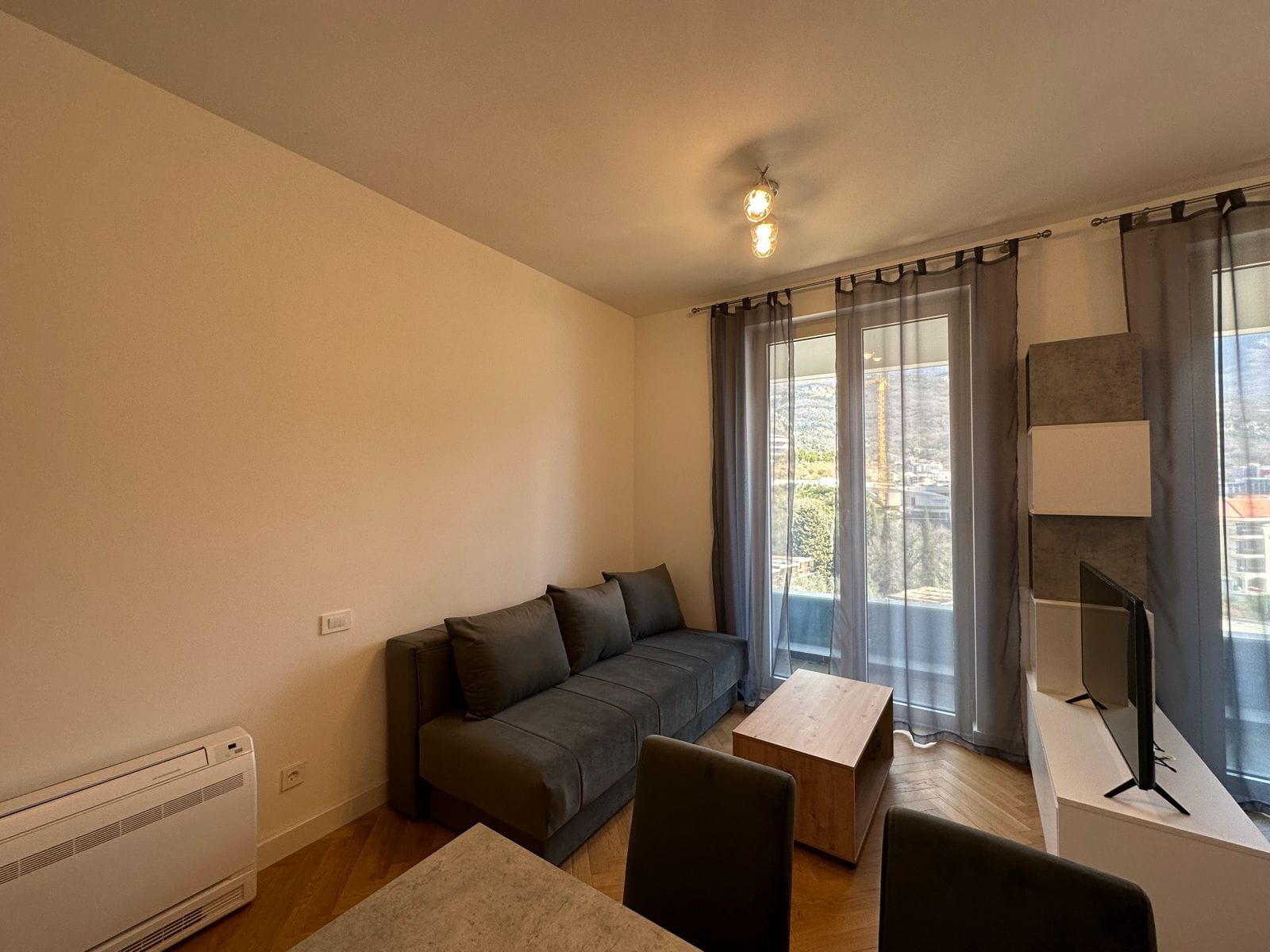 Living room in a modern apartment in Bečići, Montenegro: gray sofa, wooden coffee table, and access to a balcony with a view.