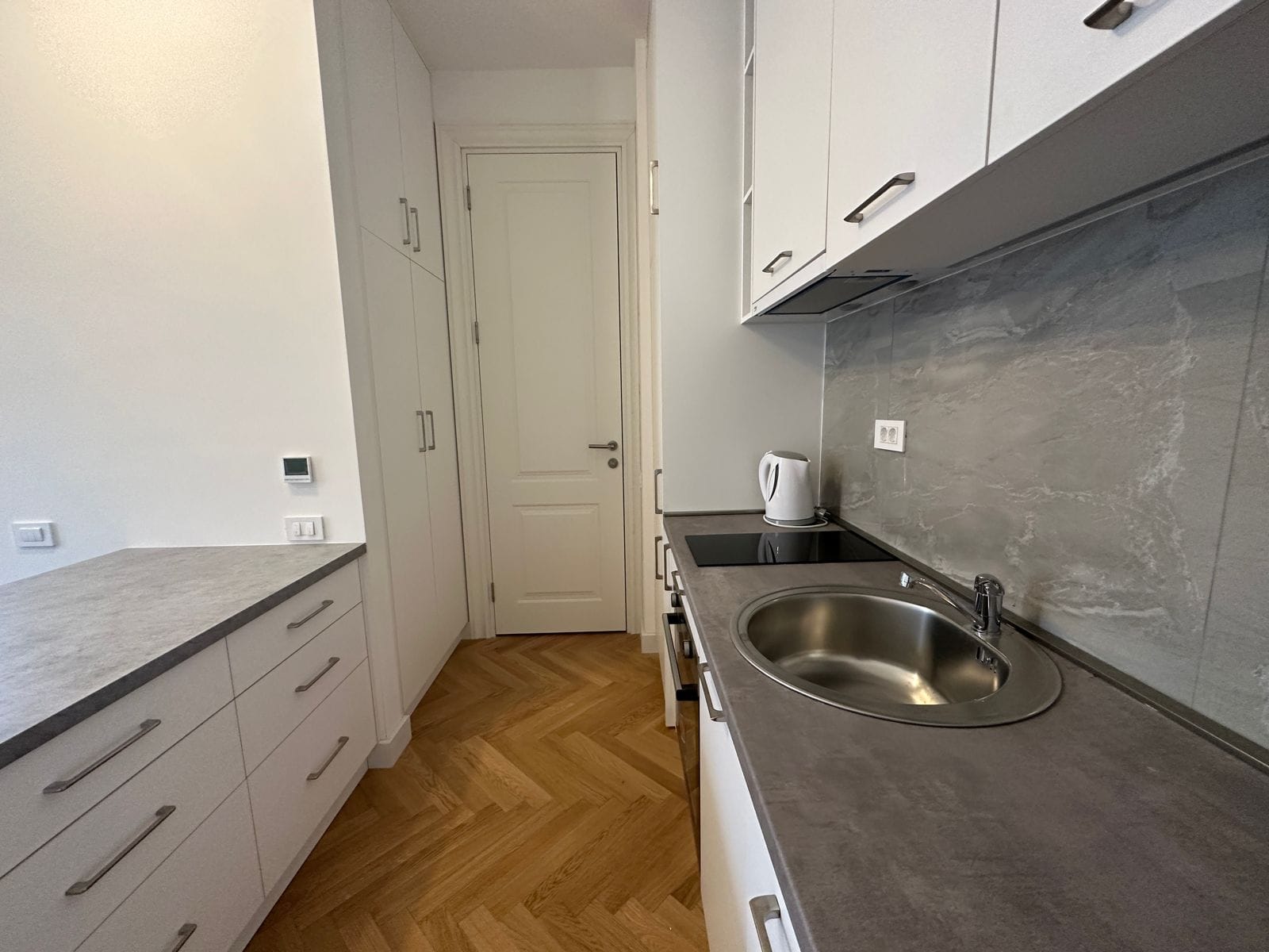 Modern kitchen in an apartment in Bečići, Montenegro: white cabinets, stone countertop, and herringbone parquet flooring.