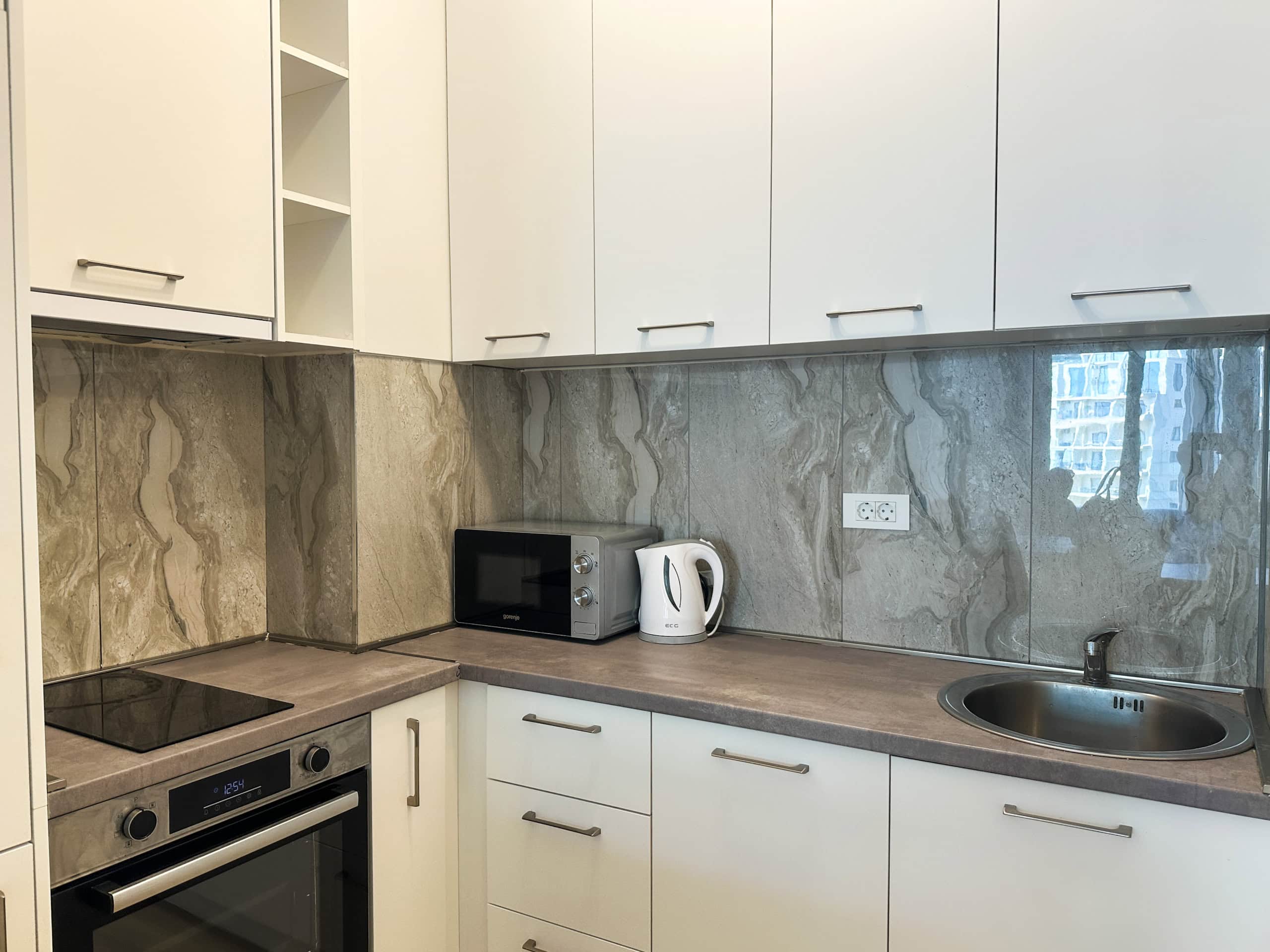 Modern white kitchen with appliances and a stone countertop in an apartment in Bečići, Montenegro