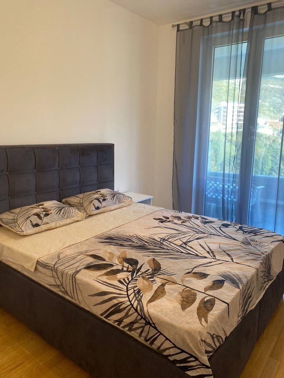 Bedroom with a double bed, botanical-print textiles, and a panoramic window in an apartment in Bečići, Montenegro