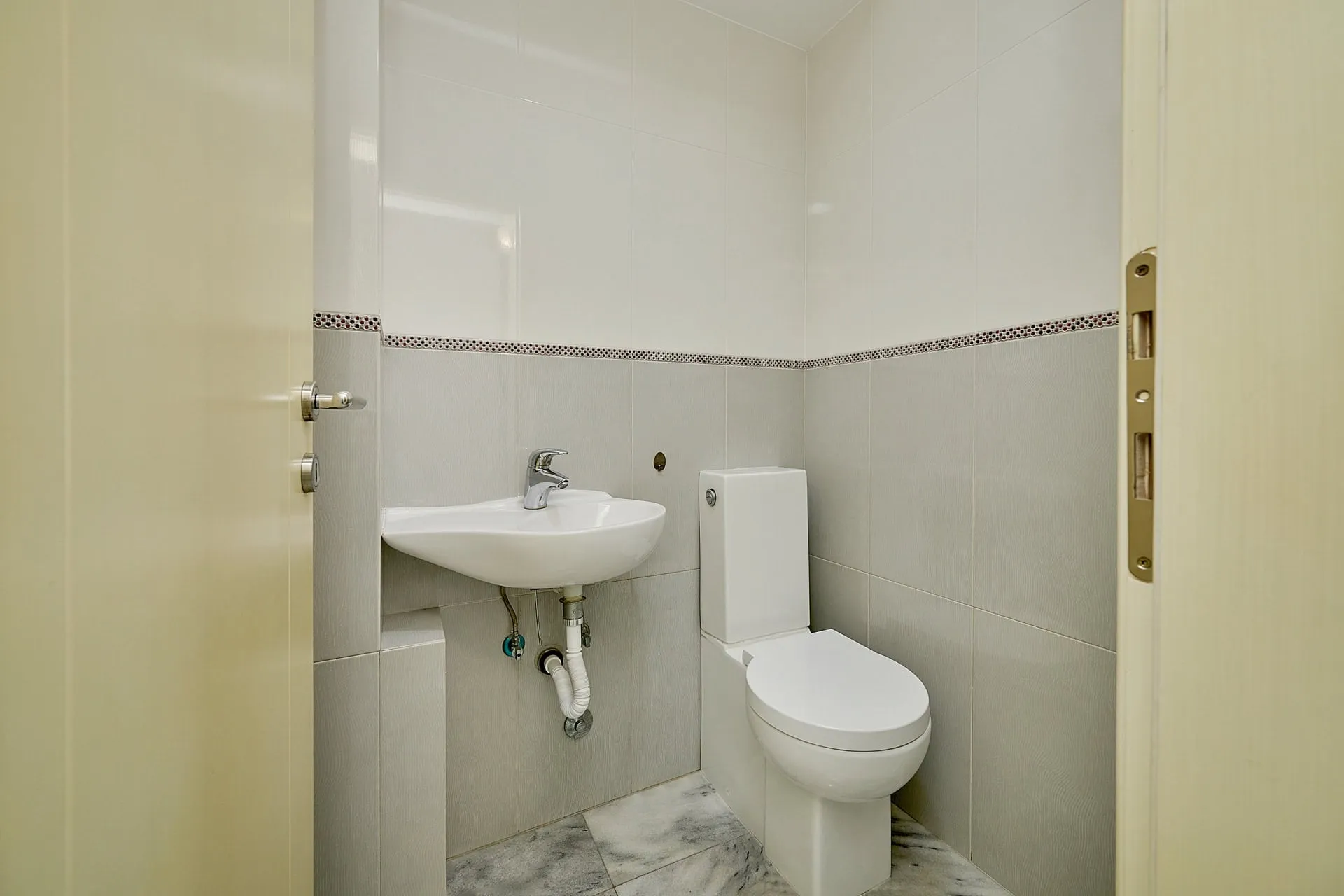 Small bathroom featuring a white toilet, wall-mounted sink with exposed plumbing, and two-tone tiled walls.