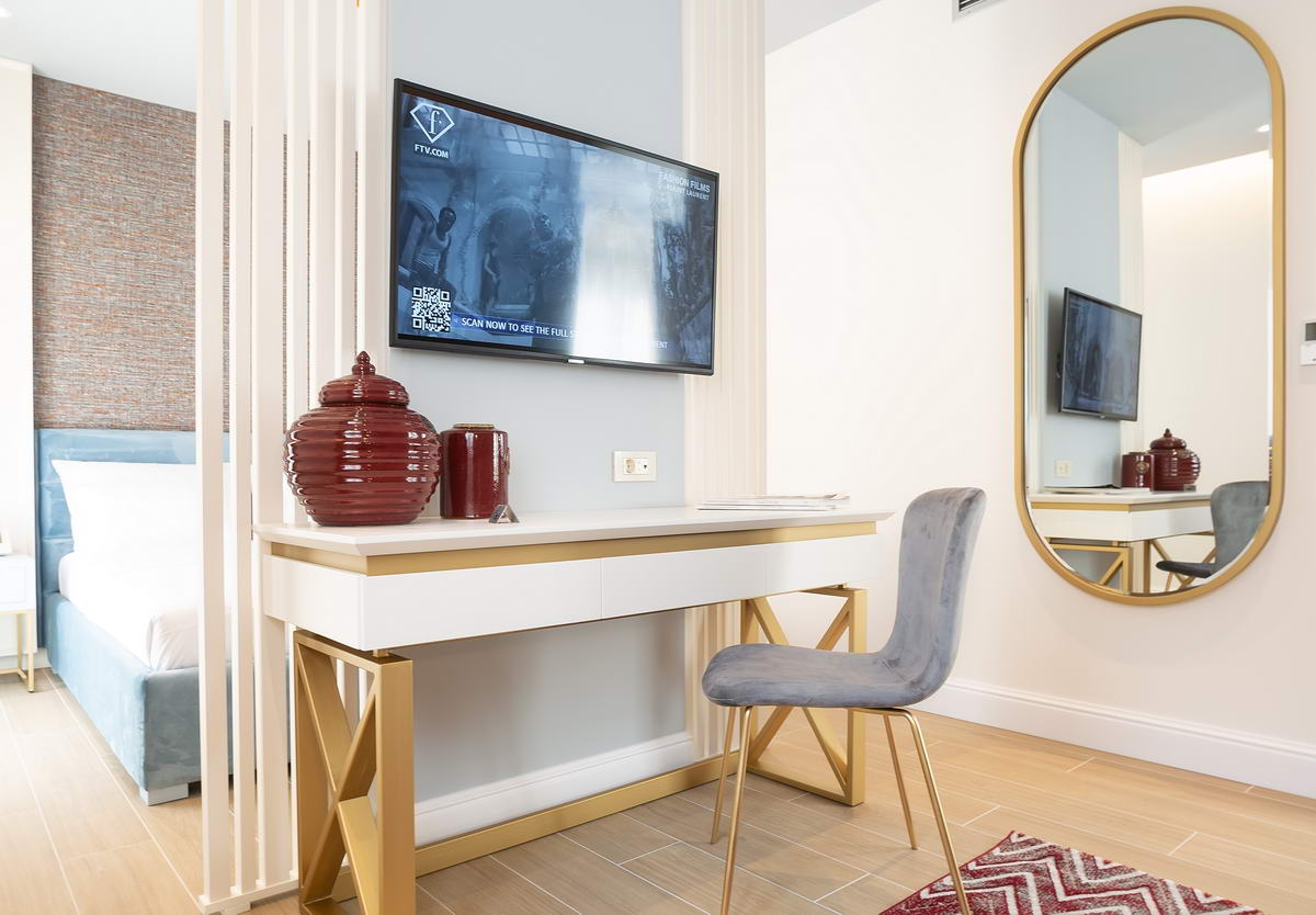 Modern hotel bedroom in Budva, Montenegro: desk, TV, large mirror, and stylish light-toned interior.
