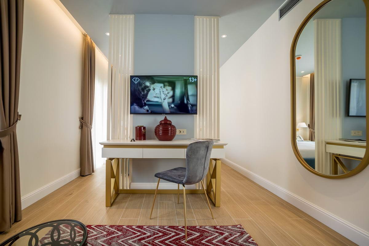 Modern hotel bedroom in Budva, Montenegro: desk, TV, stylish decor, and a large mirror in a gold frame.