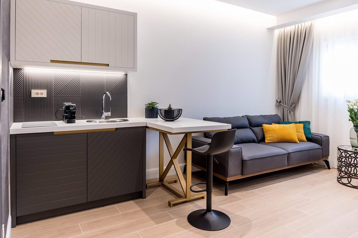 Modern studio kitchen with a bar counter and a gray sofa in a hotel in Budva, Montenegro. Stylish apartment interior.