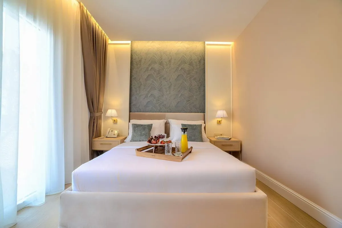 Bright bedroom featuring a large bed with a breakfast tray, nightstands, wall lamps, and a decorative patterned headboard wall.