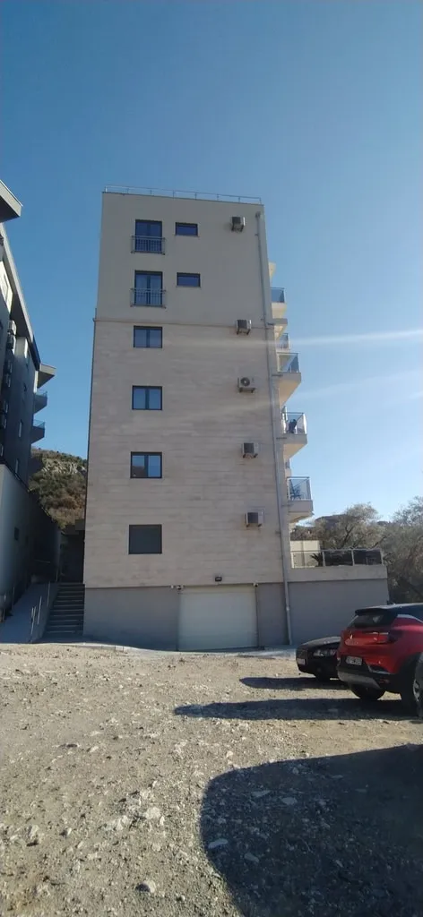 Exterior view of a multi-story residential building with balconies, AC units, and a garage under a clear blue sky.