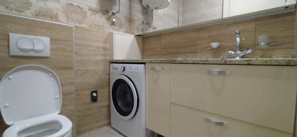Modern bathroom in an apartment, Bečići, Montenegro: beige tiles, washing machine, and a vanity unit with a sink.