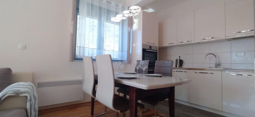 Modern kitchen-dining room in an apartment in Bečići, Montenegro: glossy kitchen set, dining table, and stylish lighting.