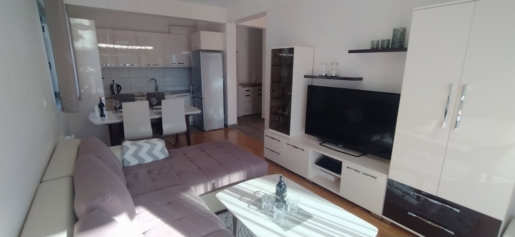 Modern living room with kitchen in an apartment in Bečići, Montenegro: corner sofa, glossy furniture, and dining area.