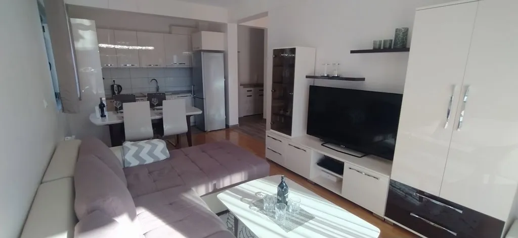 Living room featuring a sofa, TV unit, and an open kitchen area visible in the background.