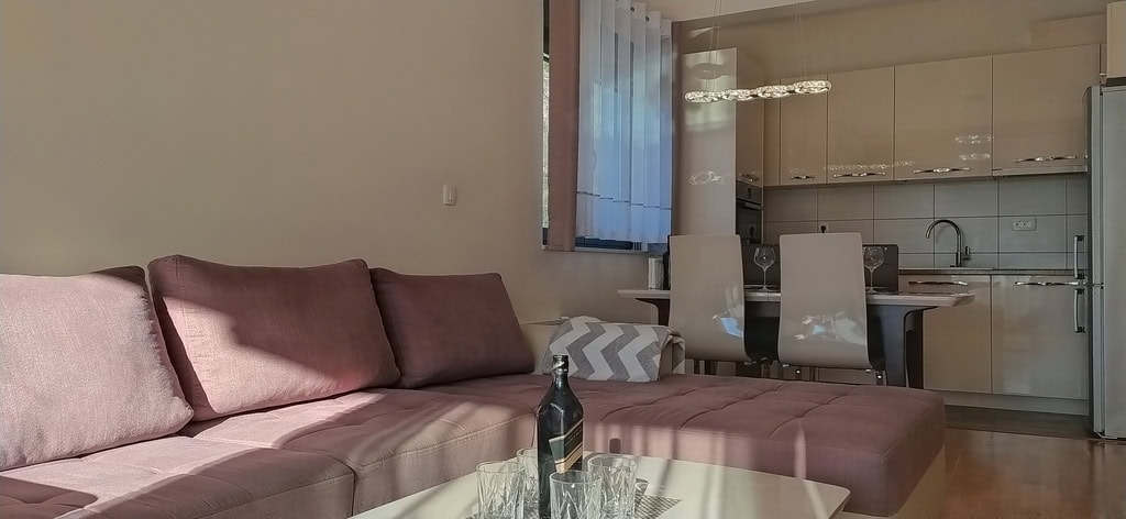 Modern living room with a pink sofa and kitchen in an apartment in Bečići, Montenegro: stylish interior and dining area.