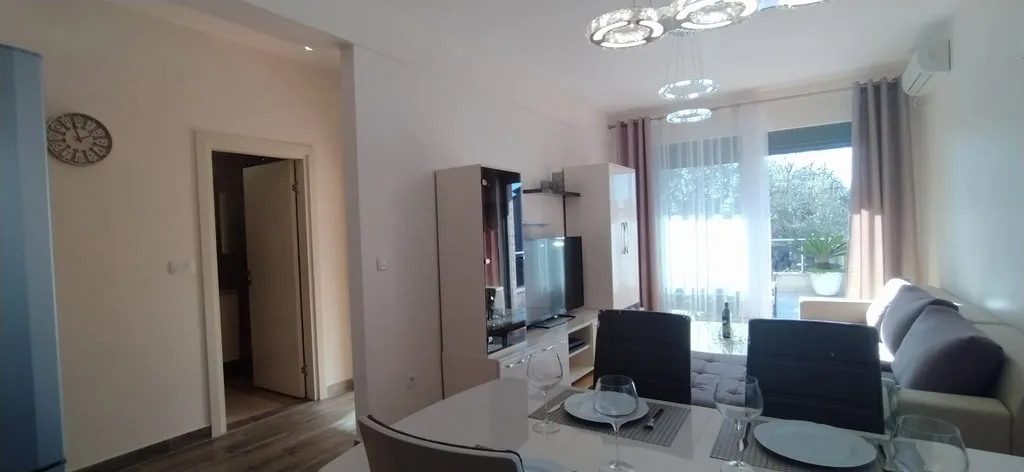 Living room with dining table, sofa, TV, and cabinet. Doorway to another room and window with balcony visible.