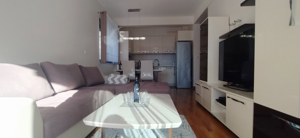 Modern living room with kitchen in an apartment in Bečići, Montenegro: corner sofa, dining area, and light-colored furniture.