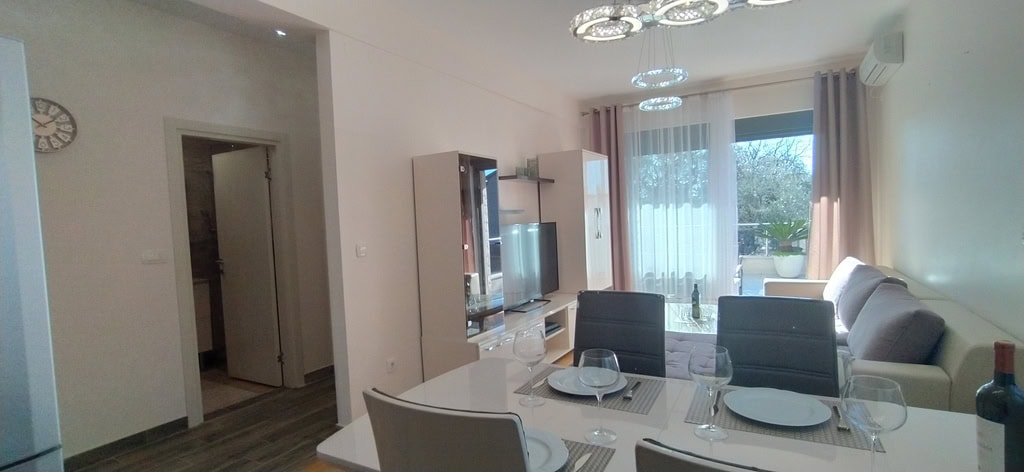 Modern living room with dining area in an apartment, Bečići, Montenegro: light furniture, TV area, and balcony access.