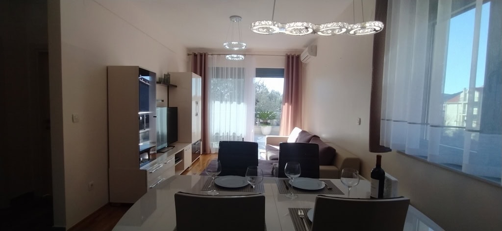 Living room with dining area in an apartment in Bečići, Montenegro: modern furniture, bright interior, and access to the terrace.