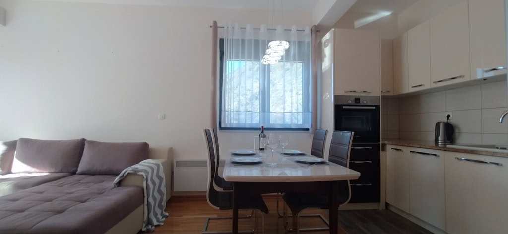 Modern living room with kitchen in an apartment in Bečići, Montenegro: soft sofa, dining area, and mountain view from the window.