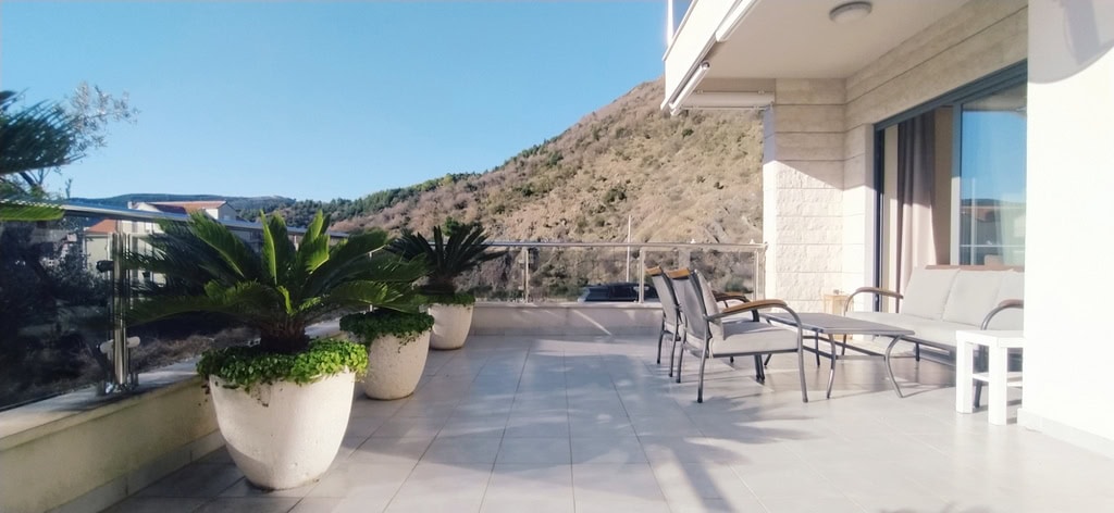 Spacious terrace with furniture and mountain views in an apartment in Bečići, Montenegro: a cozy relaxation area with plants.