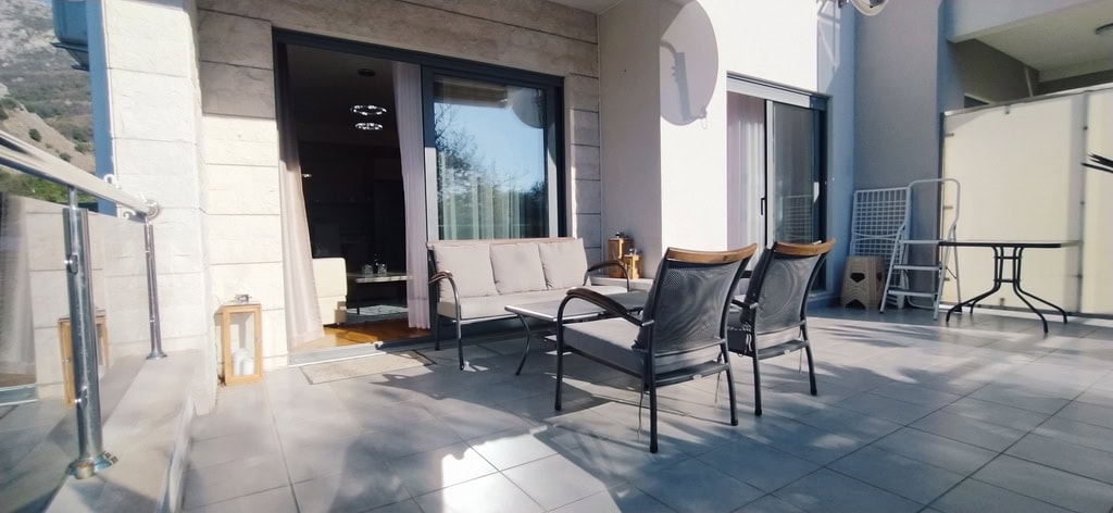 Spacious terrace with garden furniture in an apartment in Bečići, Montenegro: tiled floor, mountain view, and panoramic windows.