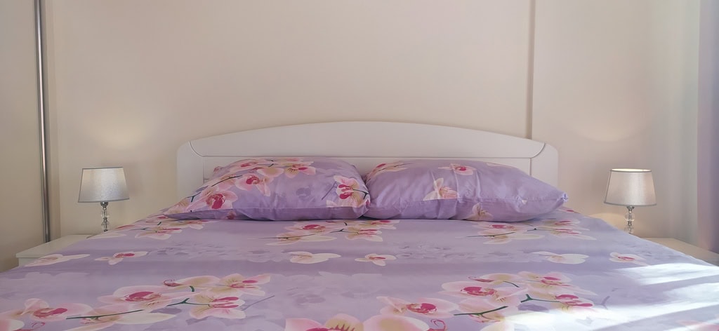 Cozy bedroom with a double bed in an apartment in Bečići, Montenegro: bright interior and bedside lamps.