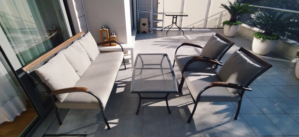 Cozy terrace with garden furniture in an apartment in Bečići, Montenegro: sofa, armchairs, and a table on a sunny balcony.