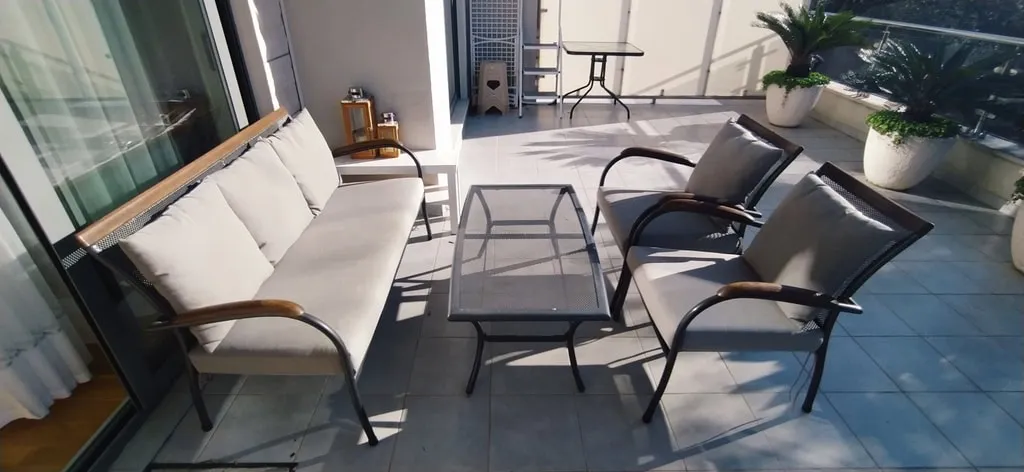 Open balcony featuring outdoor furniture including a sofa, two chairs, and a glass table on tiled flooring.