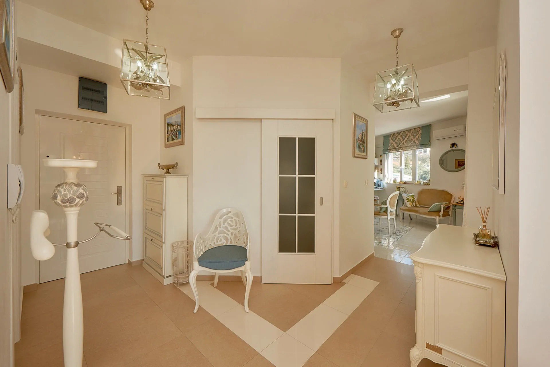 Entryway featuring a front door, white cabinet, decorative chair with blue cushion, and glass pendant lights.
