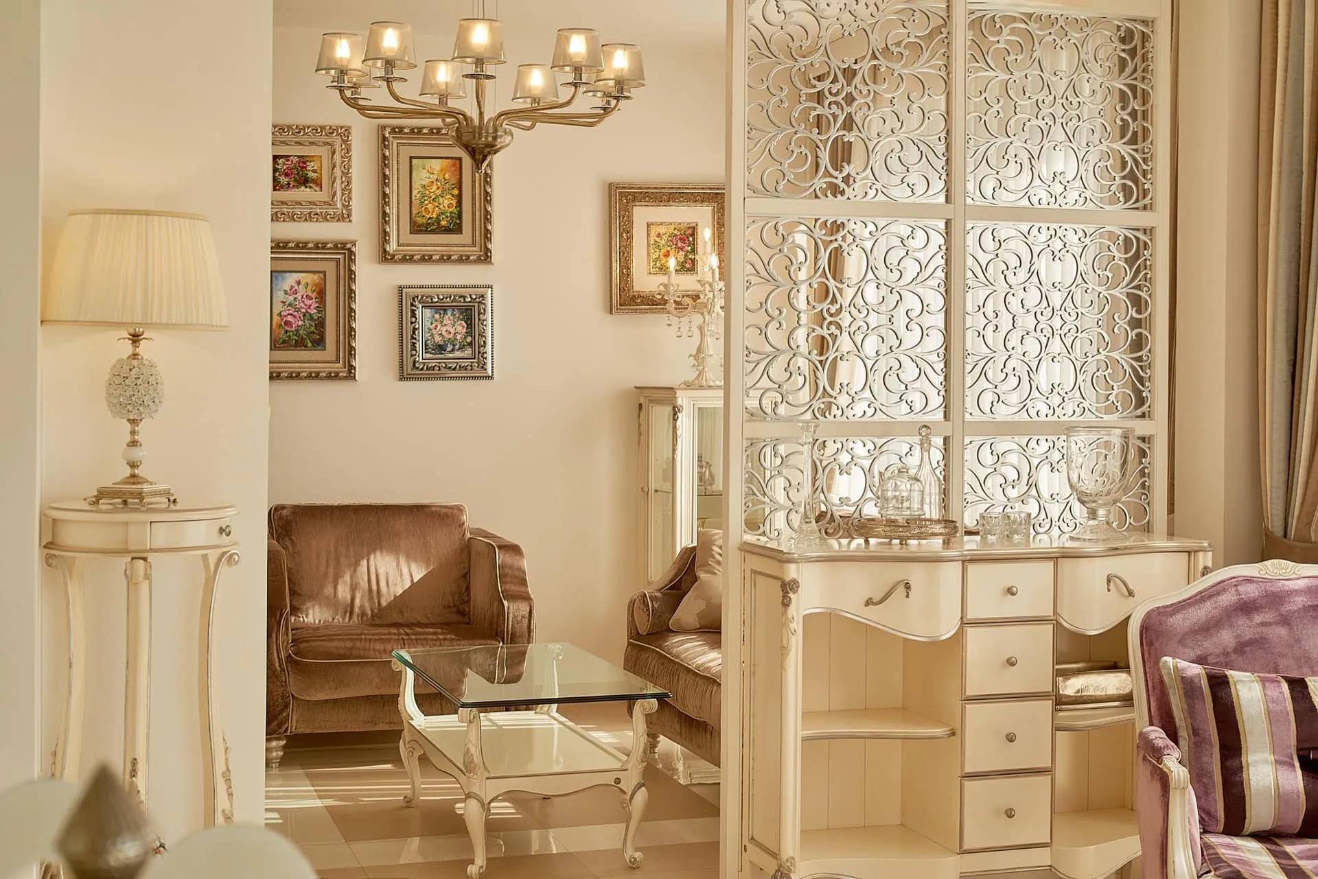 Bright classic living room featuring velvet sofas, a glass coffee table, ornate chandelier, and decorative screen.