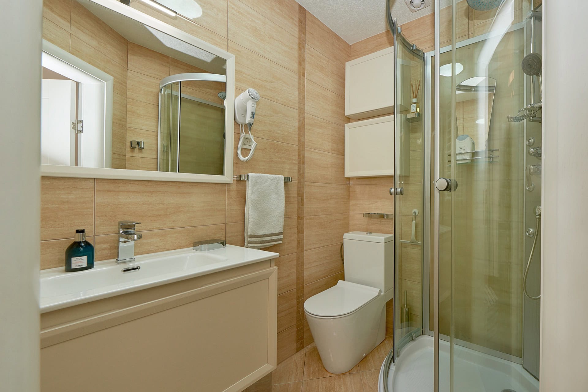 Modern bathroom with a shower cabin in a penthouse, Bečići, Montenegro: beige tiles, vanity unit, and mirror.
