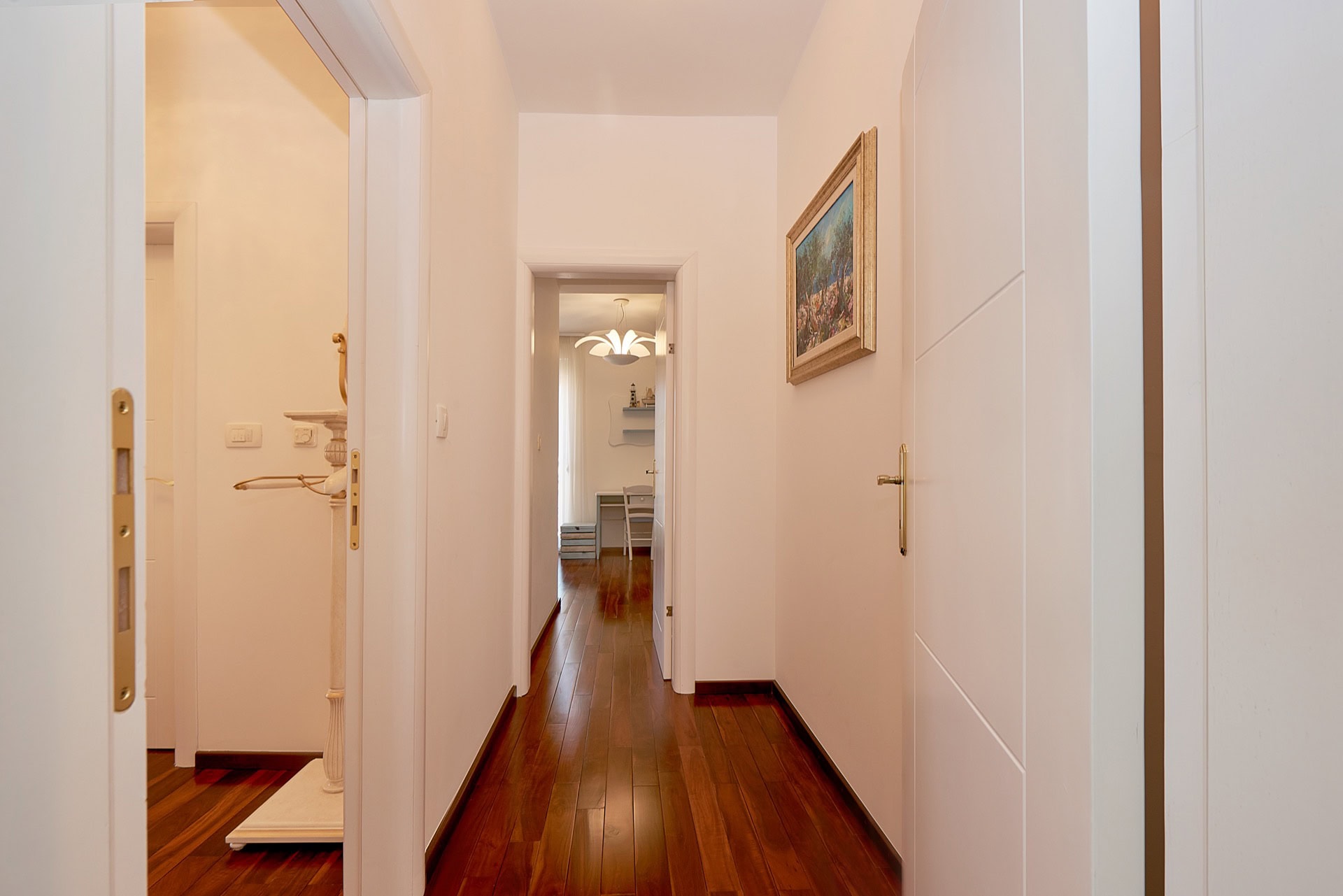 Bright hallway with parquet flooring in a penthouse in Bečići, Montenegro: view of rooms with white doors and a painting.