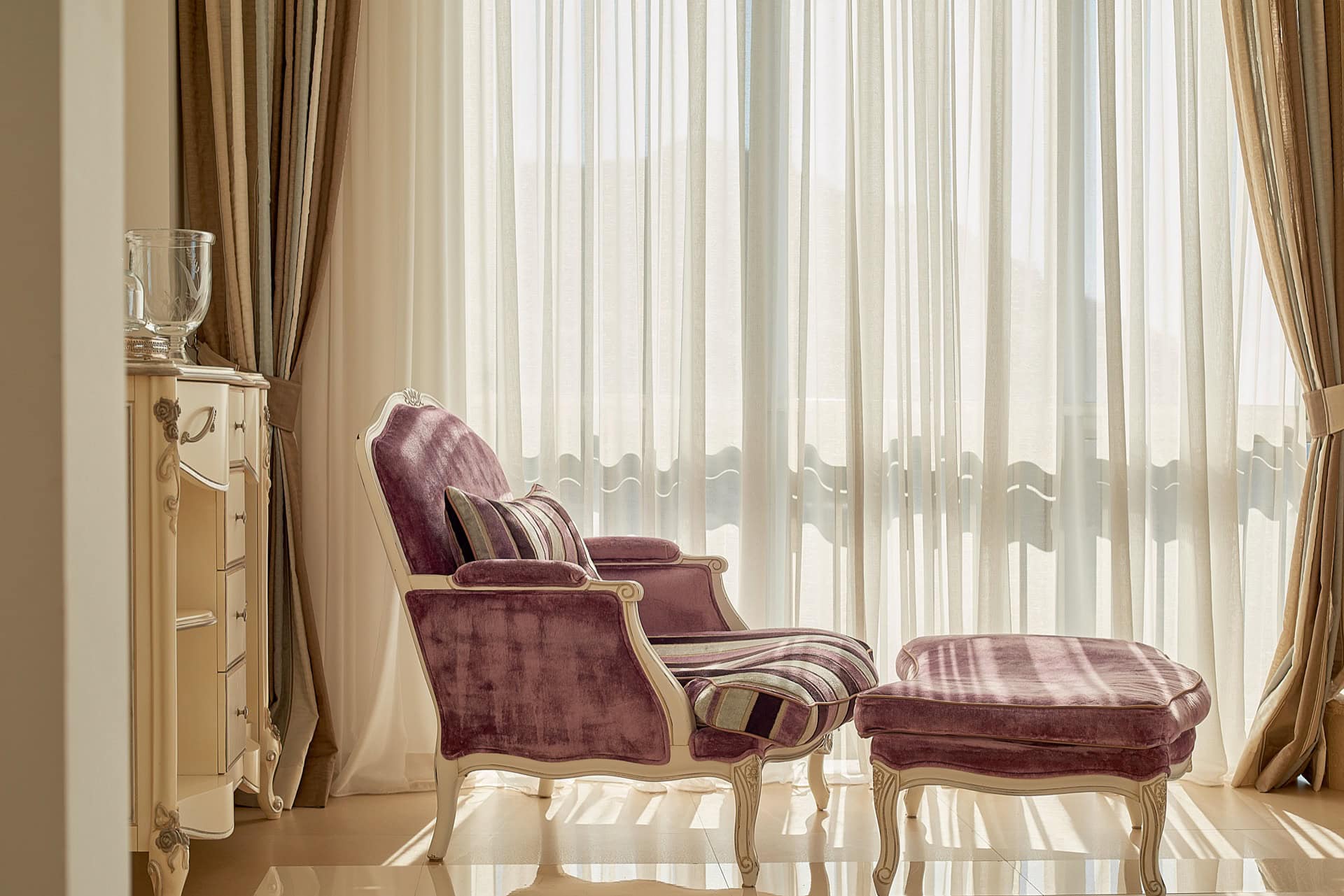 Cozy lounge area with a purple armchair and ottoman in the interior of a penthouse in Bečići, Montenegro, by the panoramic window.