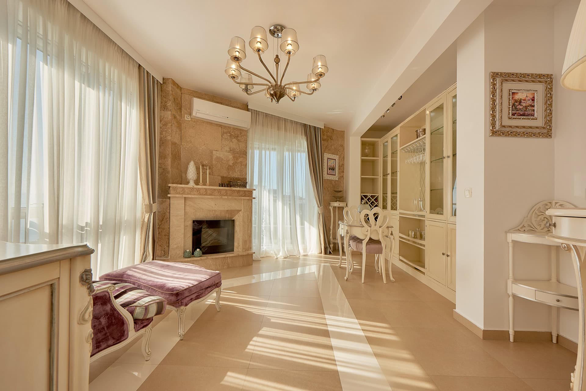 Living room in a penthouse in Bečići, Montenegro: fireplace, classic furniture, panoramic windows, and light interior finishes.