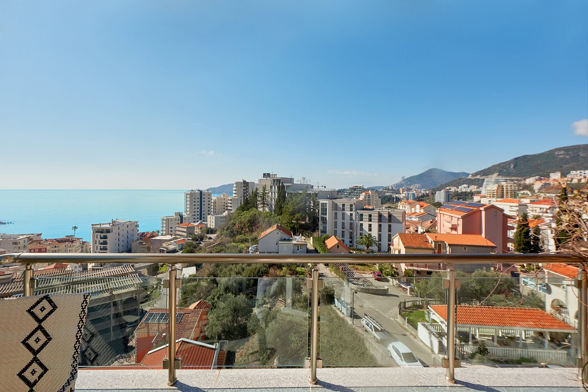 View from the penthouse balcony in Bečići, Montenegro: a panorama of the sea, mountains, and urban development with a modern terrace.