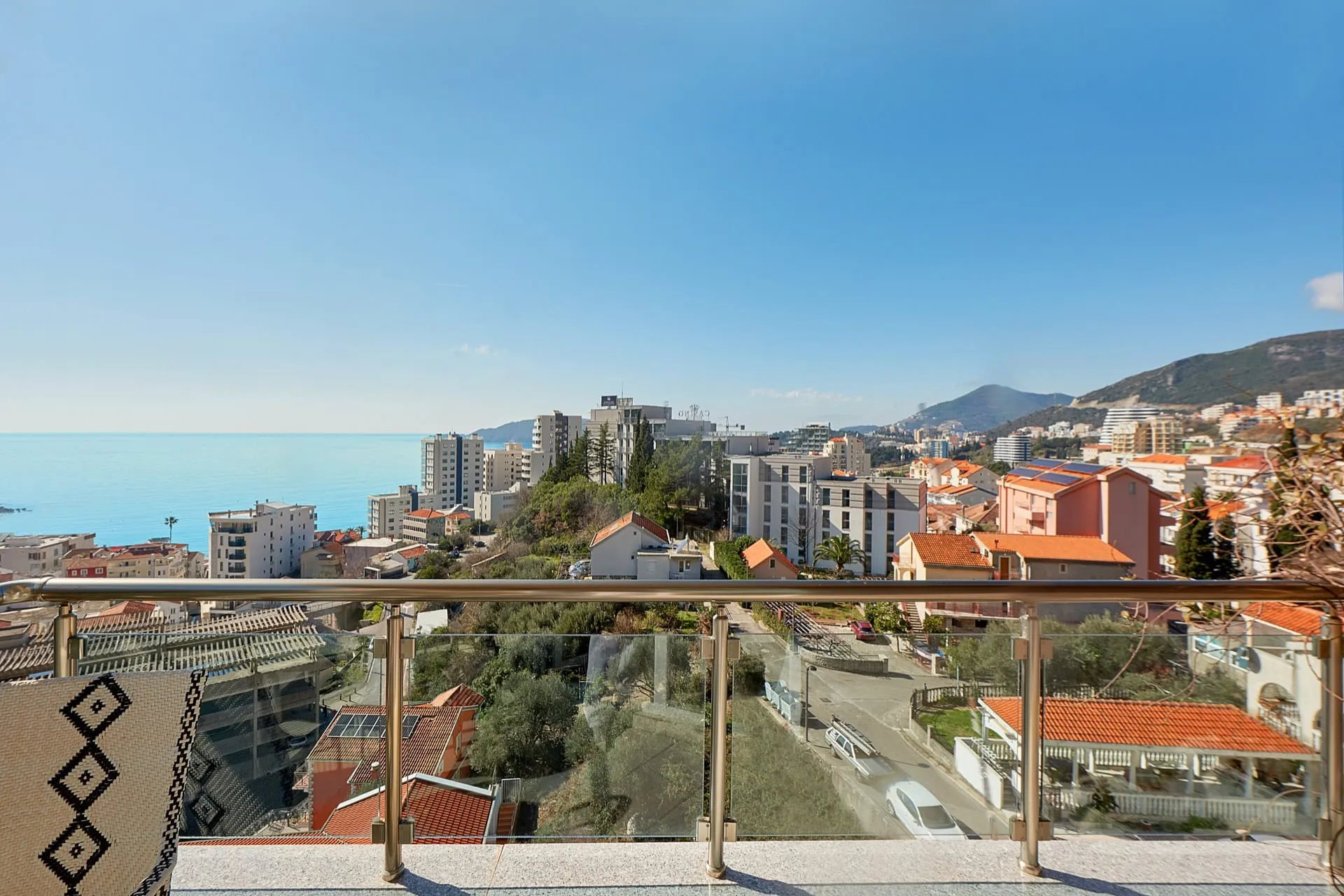 View from a balcony with glass railing overlooking the city and sea.