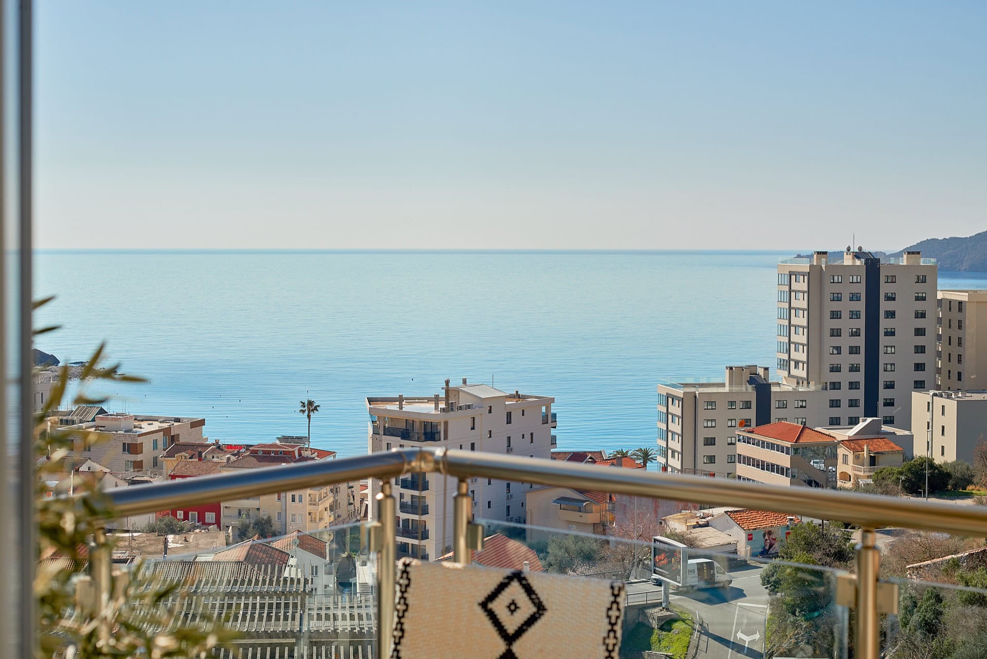 View from the penthouse balcony in Bečići, Montenegro: panorama of the Adriatic Sea, urban development, and glass railings.