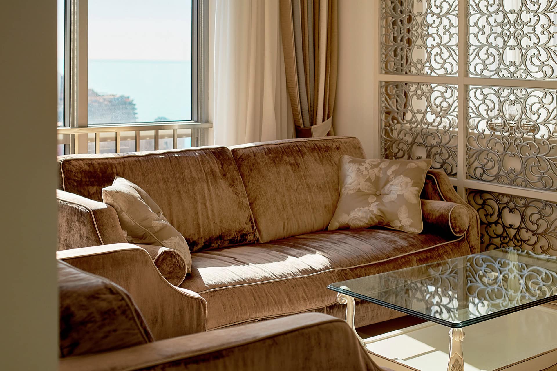 Living room in a penthouse in Bečići, Montenegro: velvet sofa, glass coffee table, and sea view through a panoramic window.