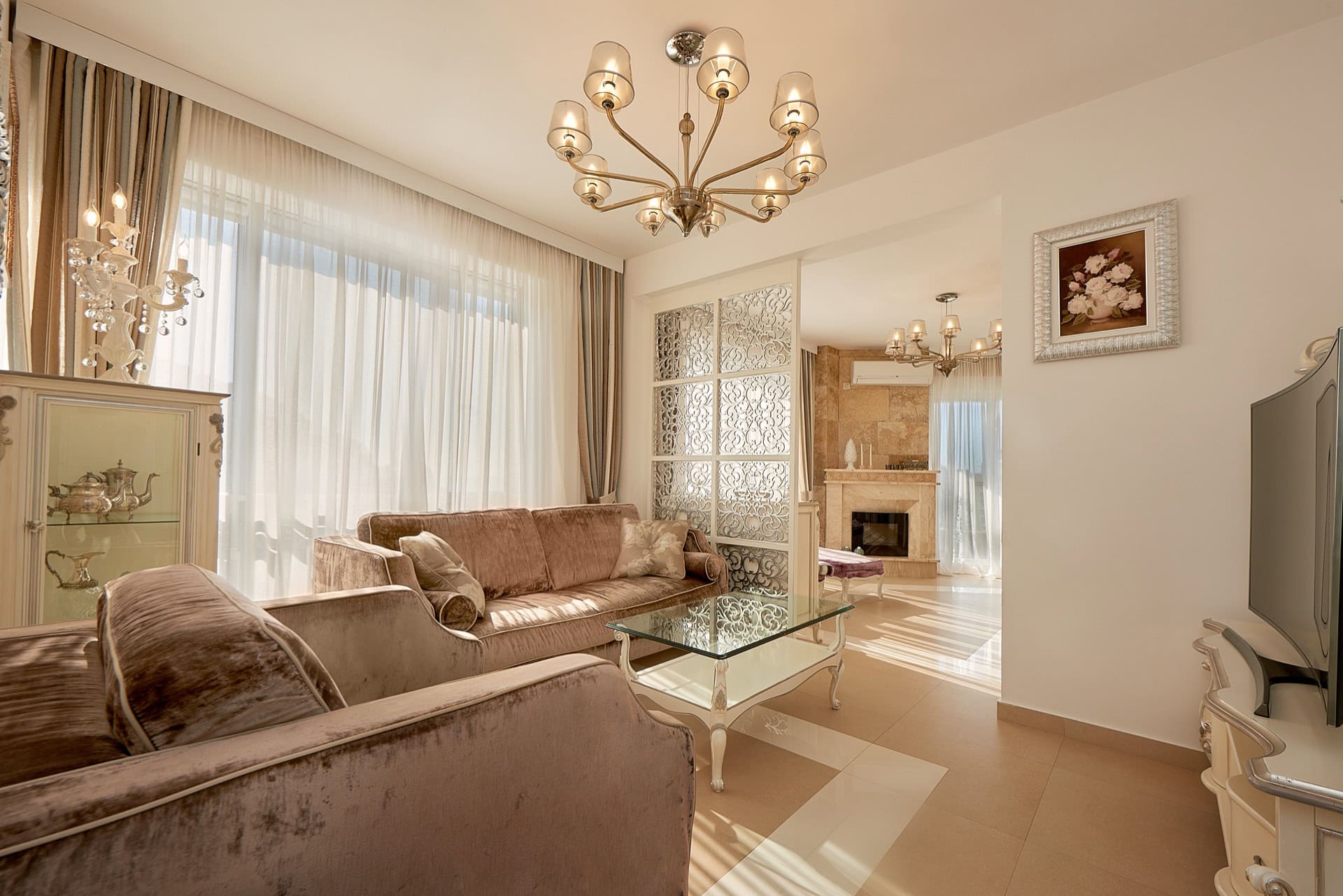 Luxurious living room with a fireplace in a penthouse, Bečići, Montenegro: upholstered furniture, decorative partition, and chandeliers.