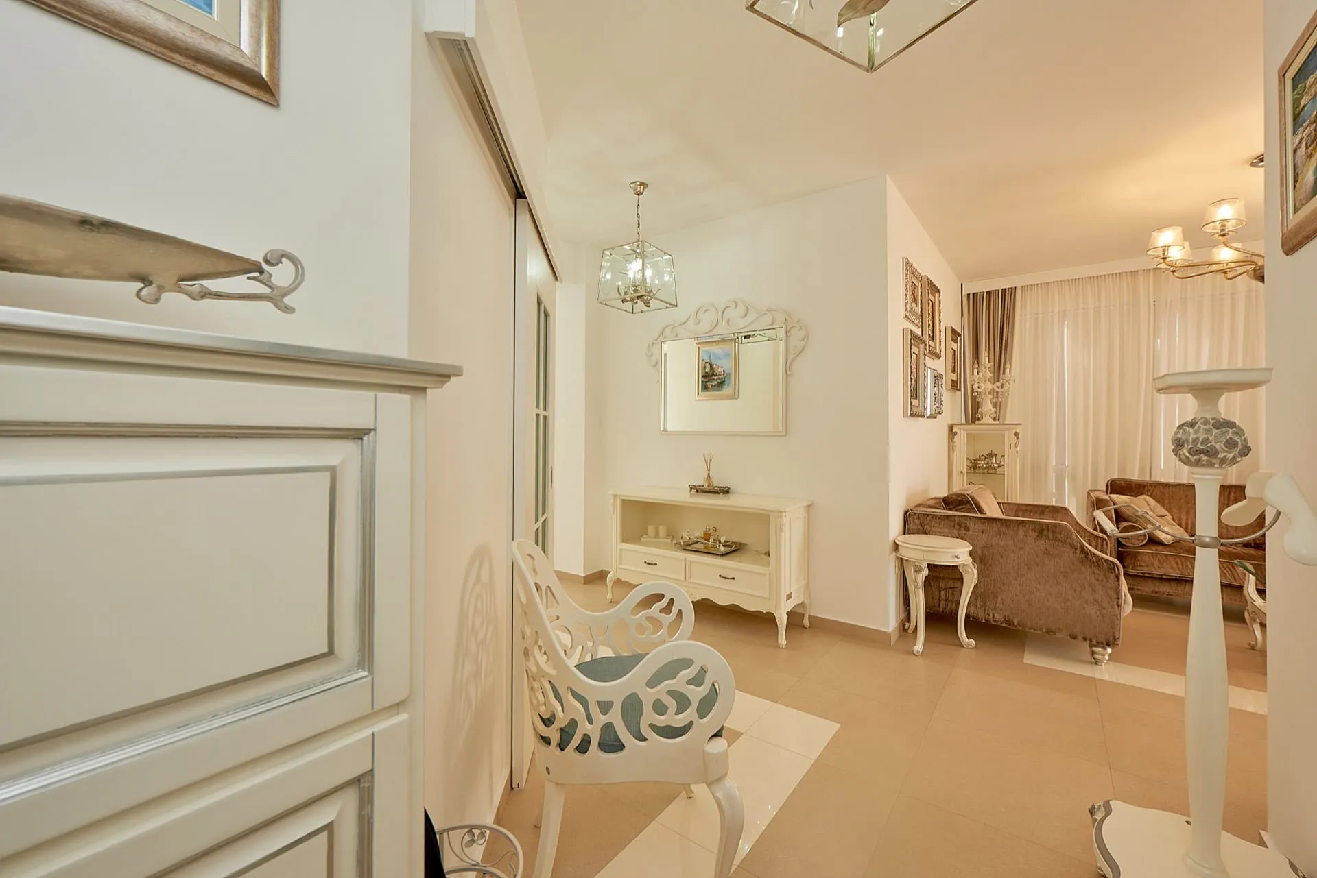 Living room featuring a white ornate chair, console table, mirror, and brown velvet sofa against light walls.