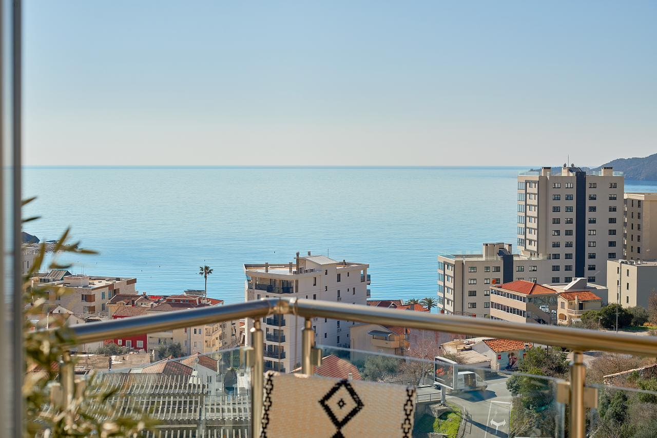 View from the penthouse balcony in Bečići, Montenegro: panorama of the Adriatic Sea, urban development, and modern buildings.