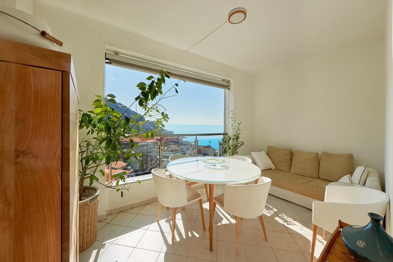 Bright balcony of a penthouse in Bečići, Montenegro, with a dining area, wicker furniture, and panoramic sea views.