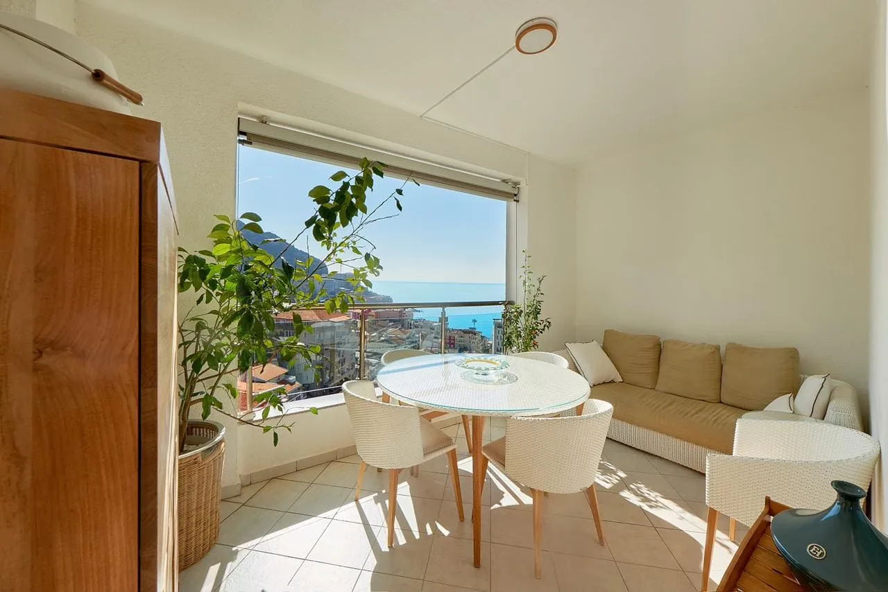 Enclosed balcony featuring a dining table, sofa, and a scenic view of the sea and city.