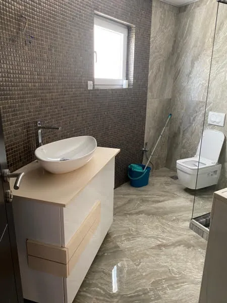 Bathroom with vessel sink on vanity, wall-mounted toilet, brown mosaic tile wall, and glass shower partition.