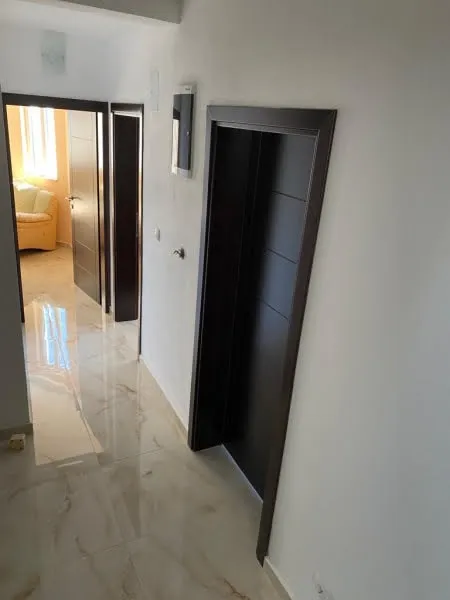 Hallway with glossy marble tiles and dark door frames. A glimpse of a room with a yellow sofa is visible through an open door.